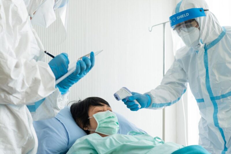 Doctor and nurse in personal protective equipment or ppe treating the asian woman patient with covid-19 or coronavirus infection in the isolation unit in the hospital during pandemic. medical concept
